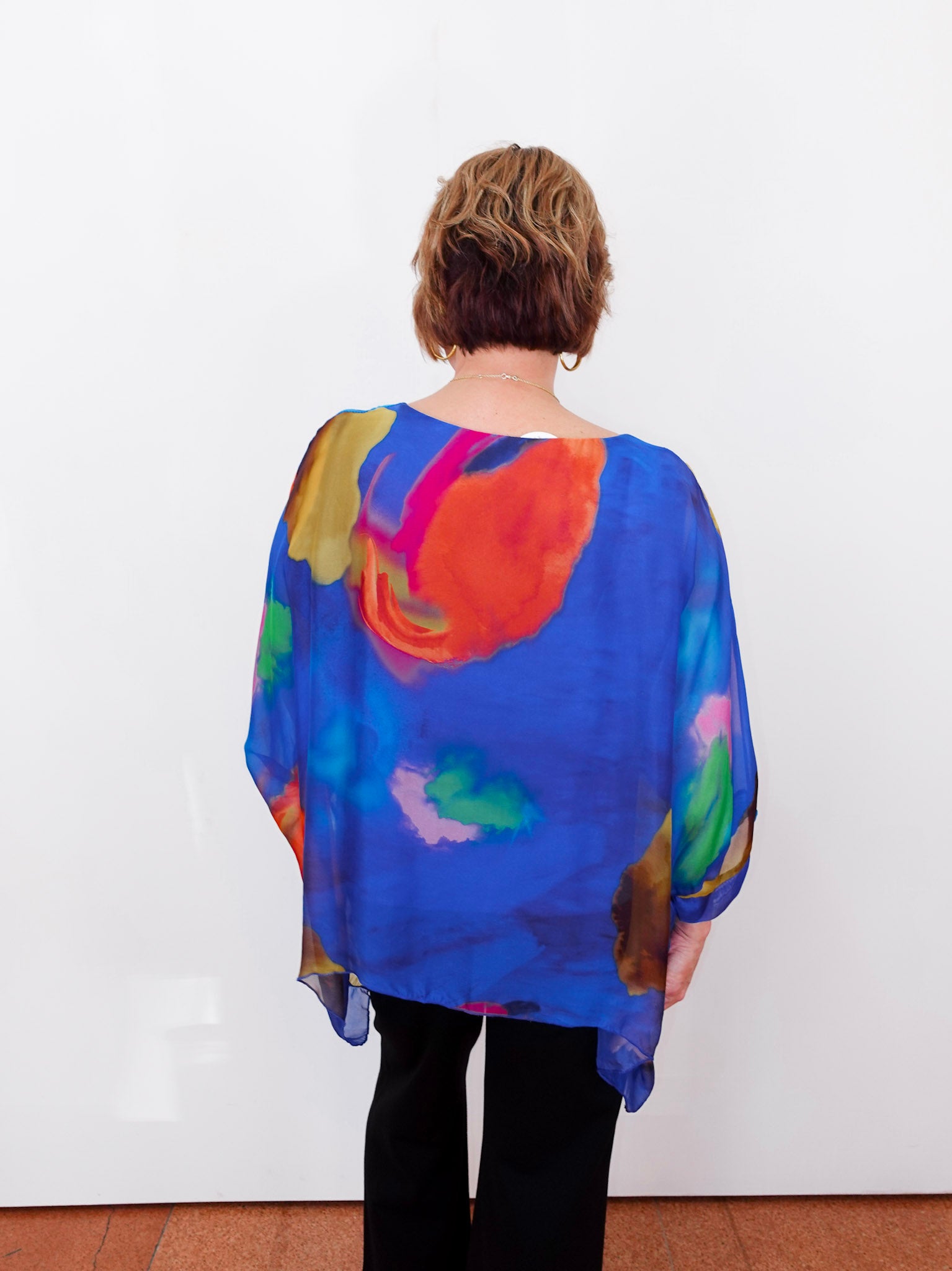 Person wearing a colorful, sheer blouse with a white background