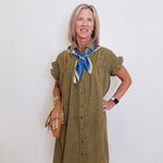 Woman wearing an olive green dress with a blue scarf against a white background