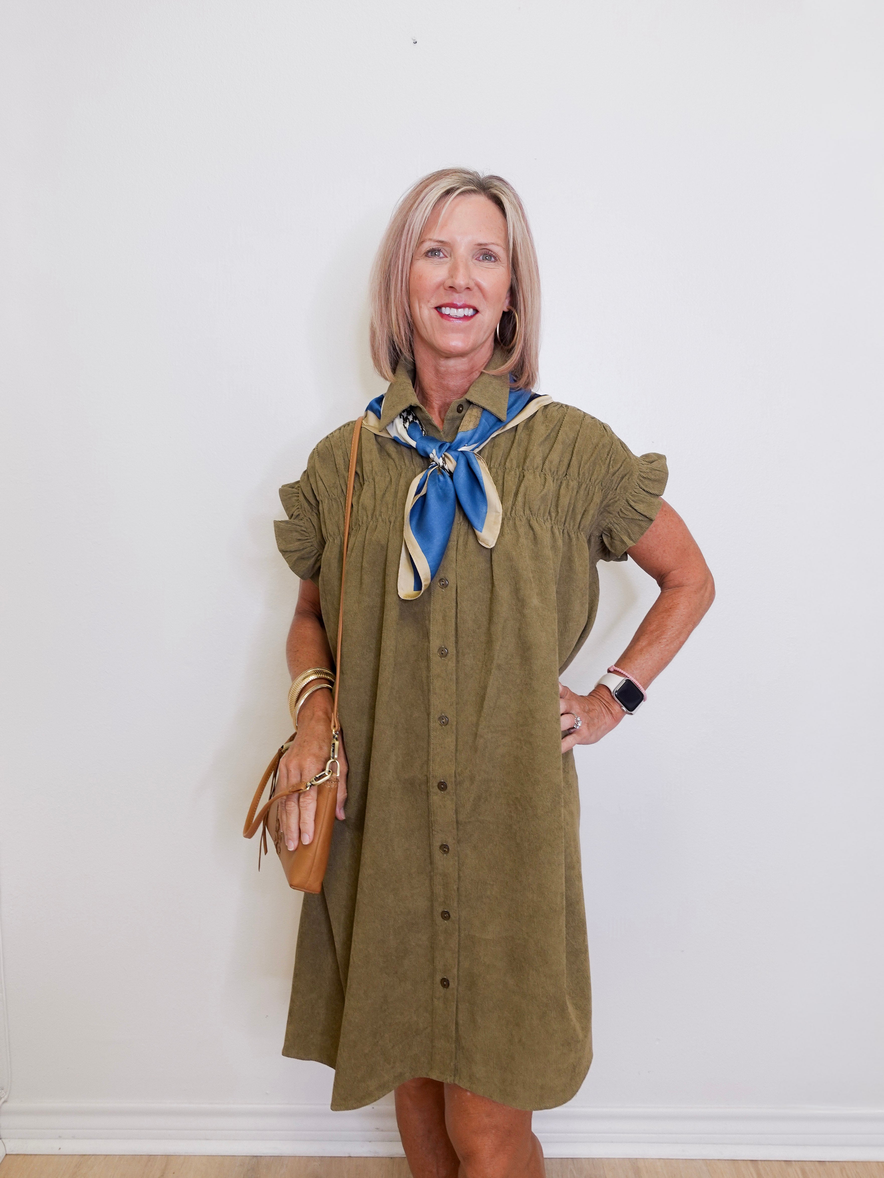 Woman wearing an olive green dress with a blue scarf against a white background