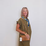 Woman wearing a green dress with a brown bag against a white wall