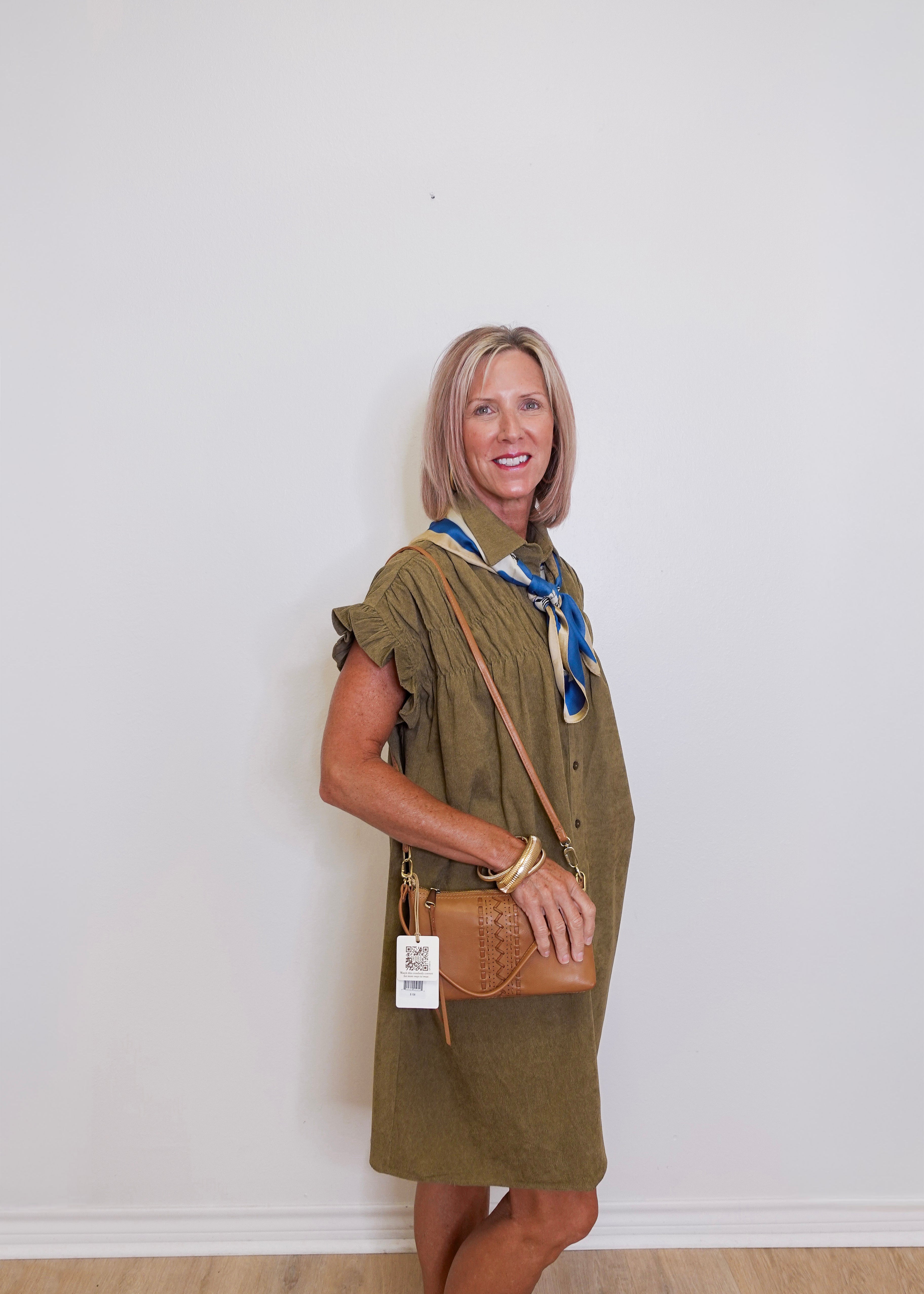 Woman wearing a green dress with a brown bag against a white wall
