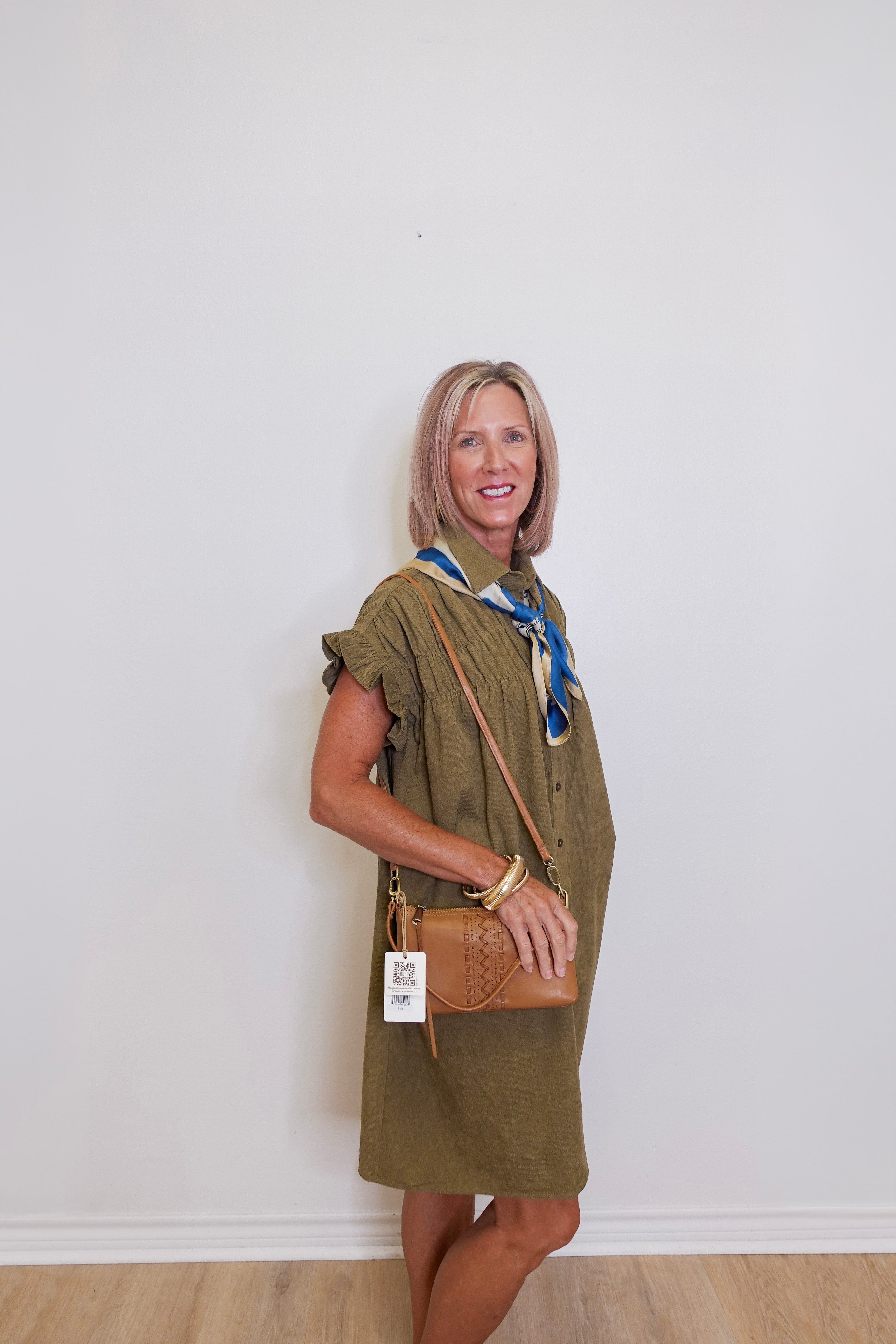 Woman wearing a green dress with a brown bag against a white wall