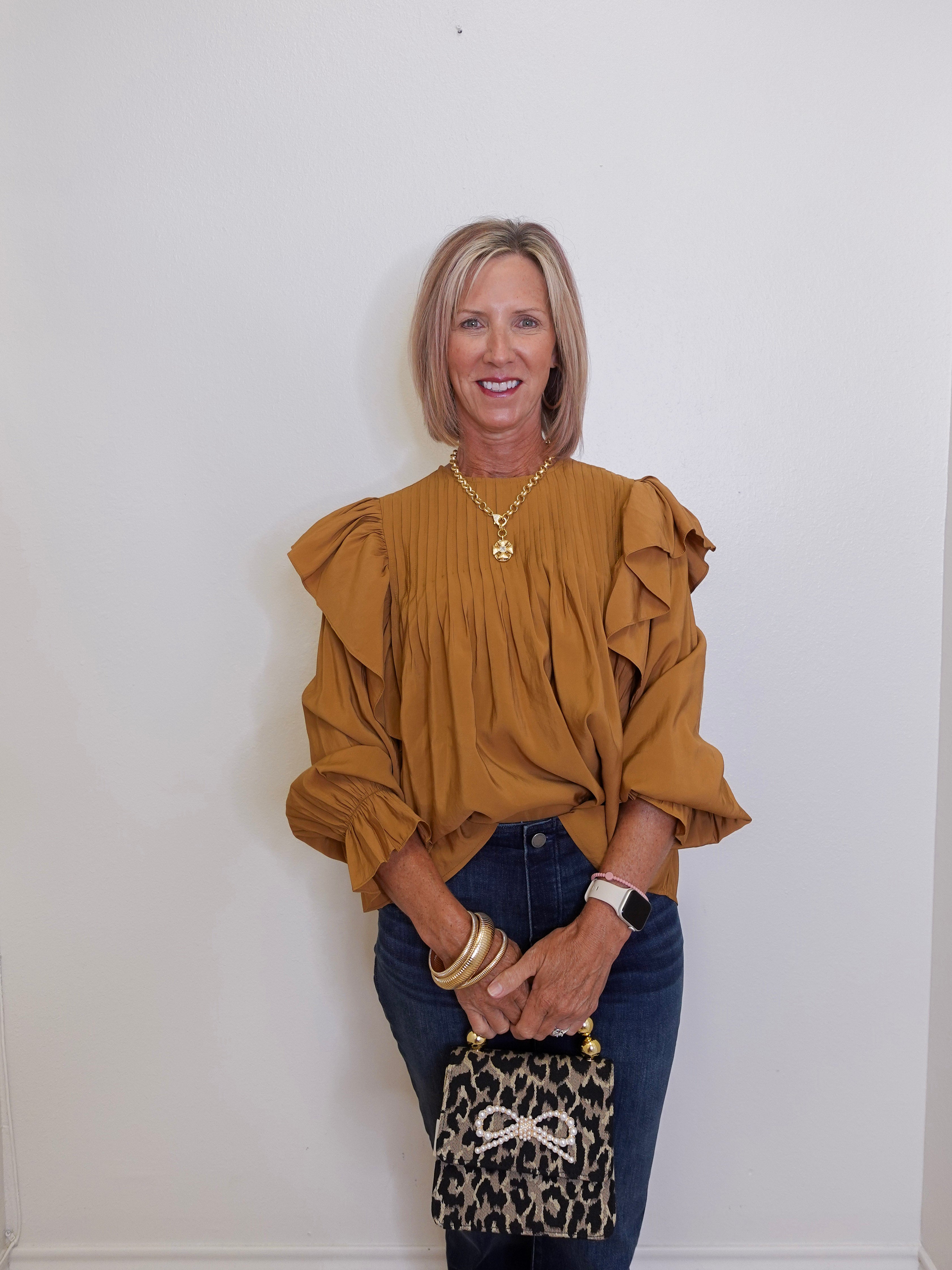 Woman wearing a mustard yellow blouse with ruffled sleeves against a white wall.