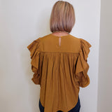 Person wearing a mustard yellow blouse with ruffled sleeves against a white wall.