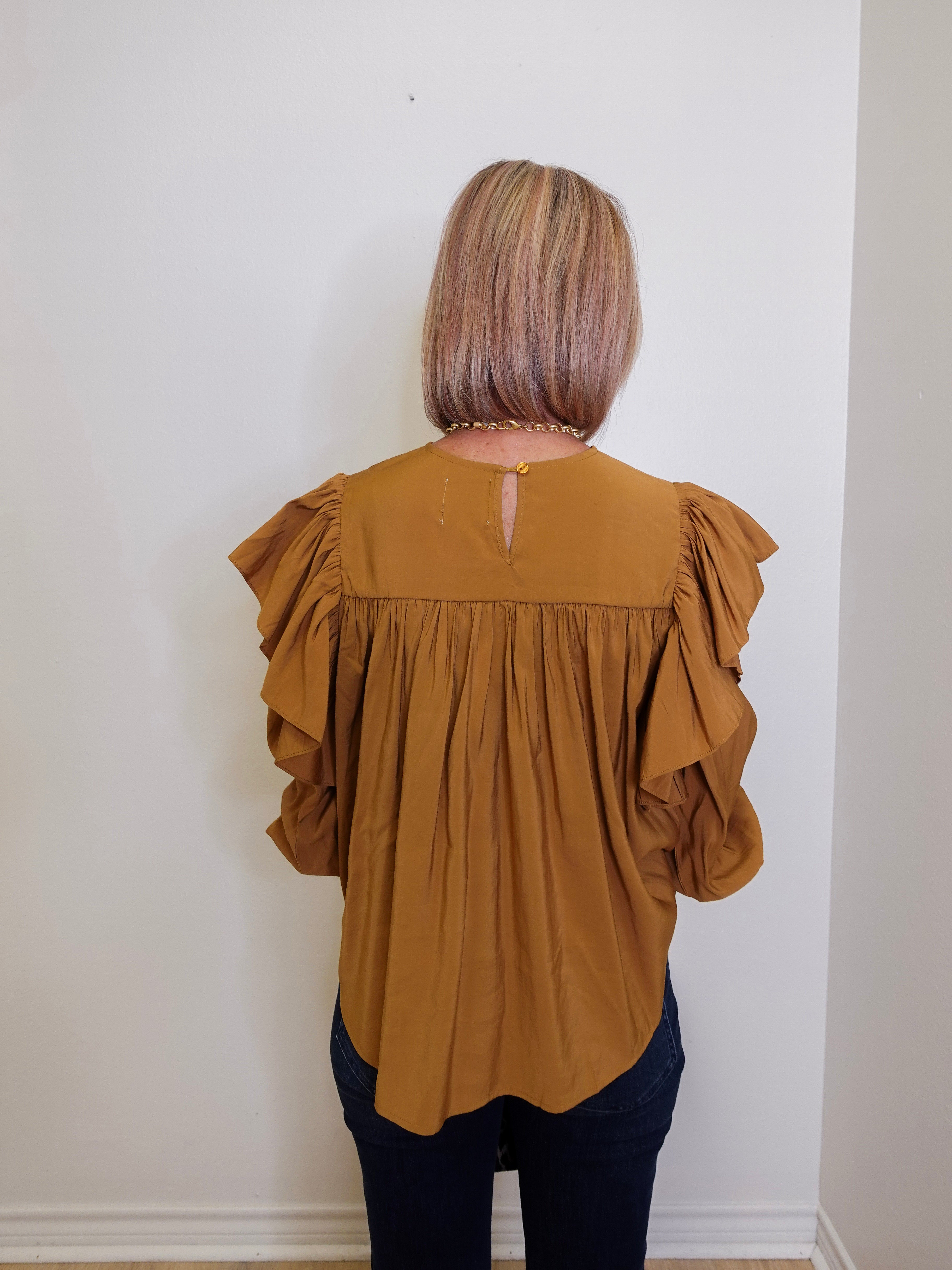 Person wearing a mustard yellow blouse with ruffled sleeves against a white wall.