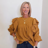 Woman wearing a mustard yellow blouse with ruffled sleeves against a white wall