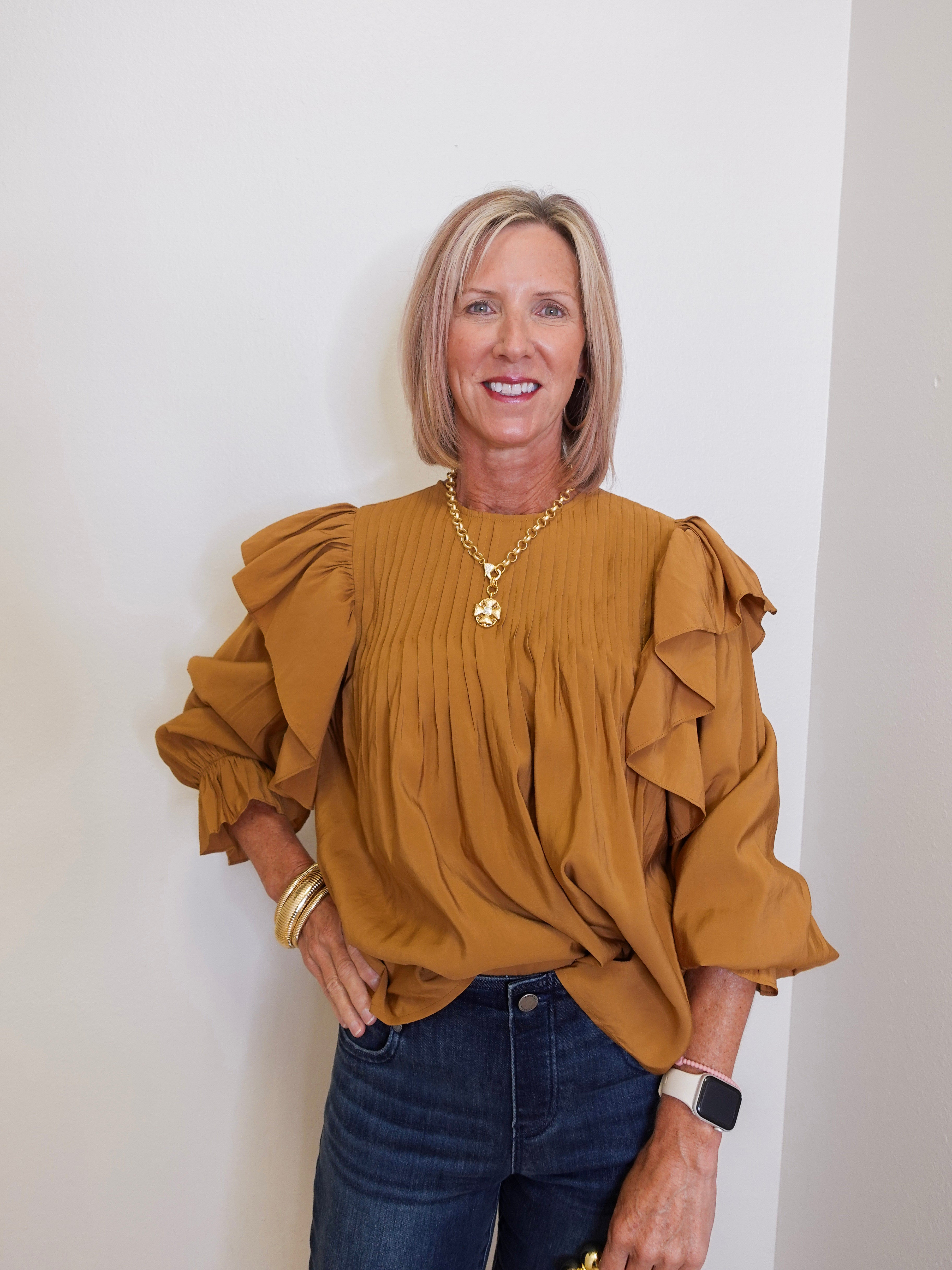 Woman wearing a mustard yellow blouse with ruffled sleeves against a white wall