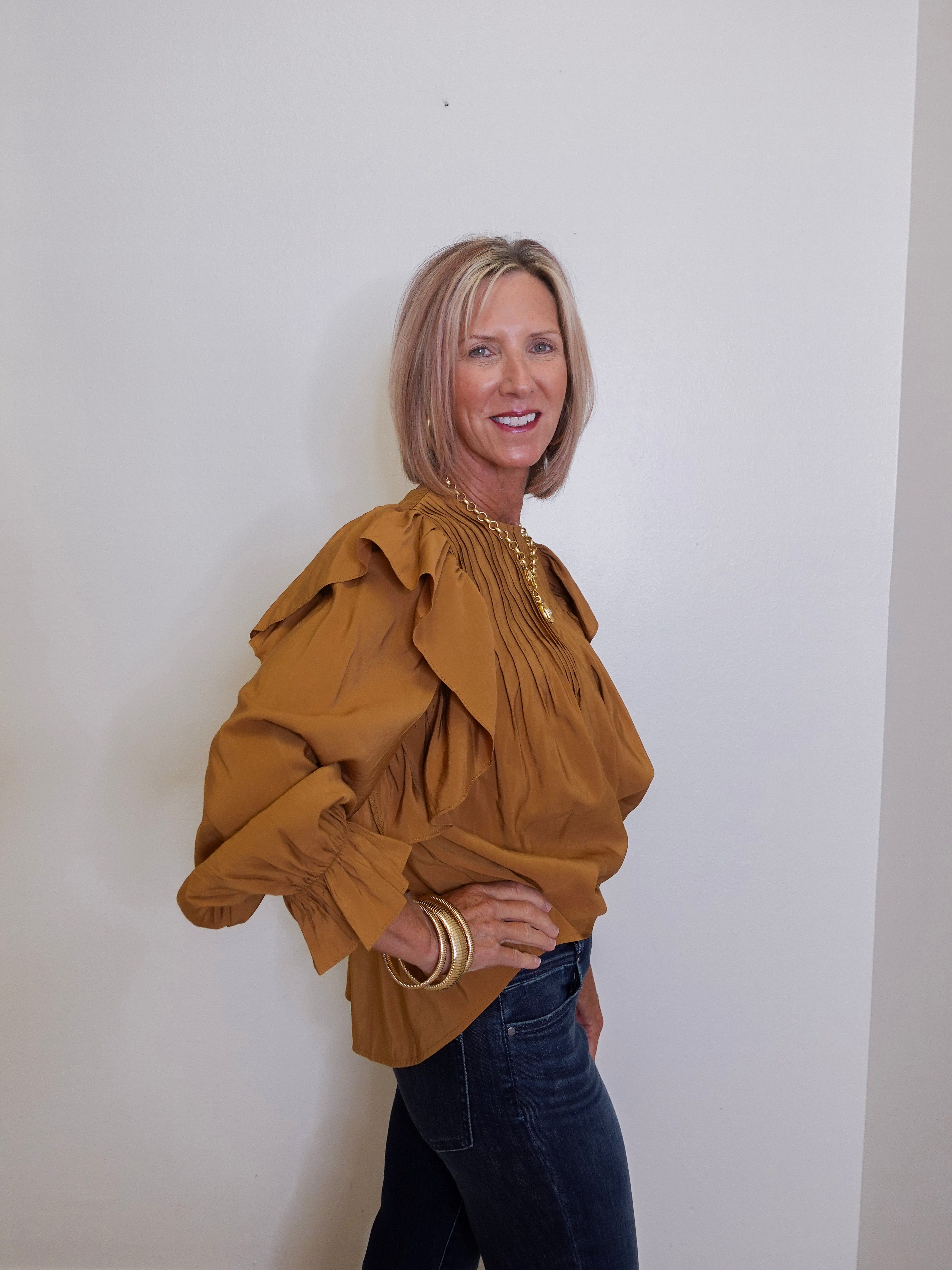 Woman wearing a mustard yellow blouse with ruffled sleeves against a white wall