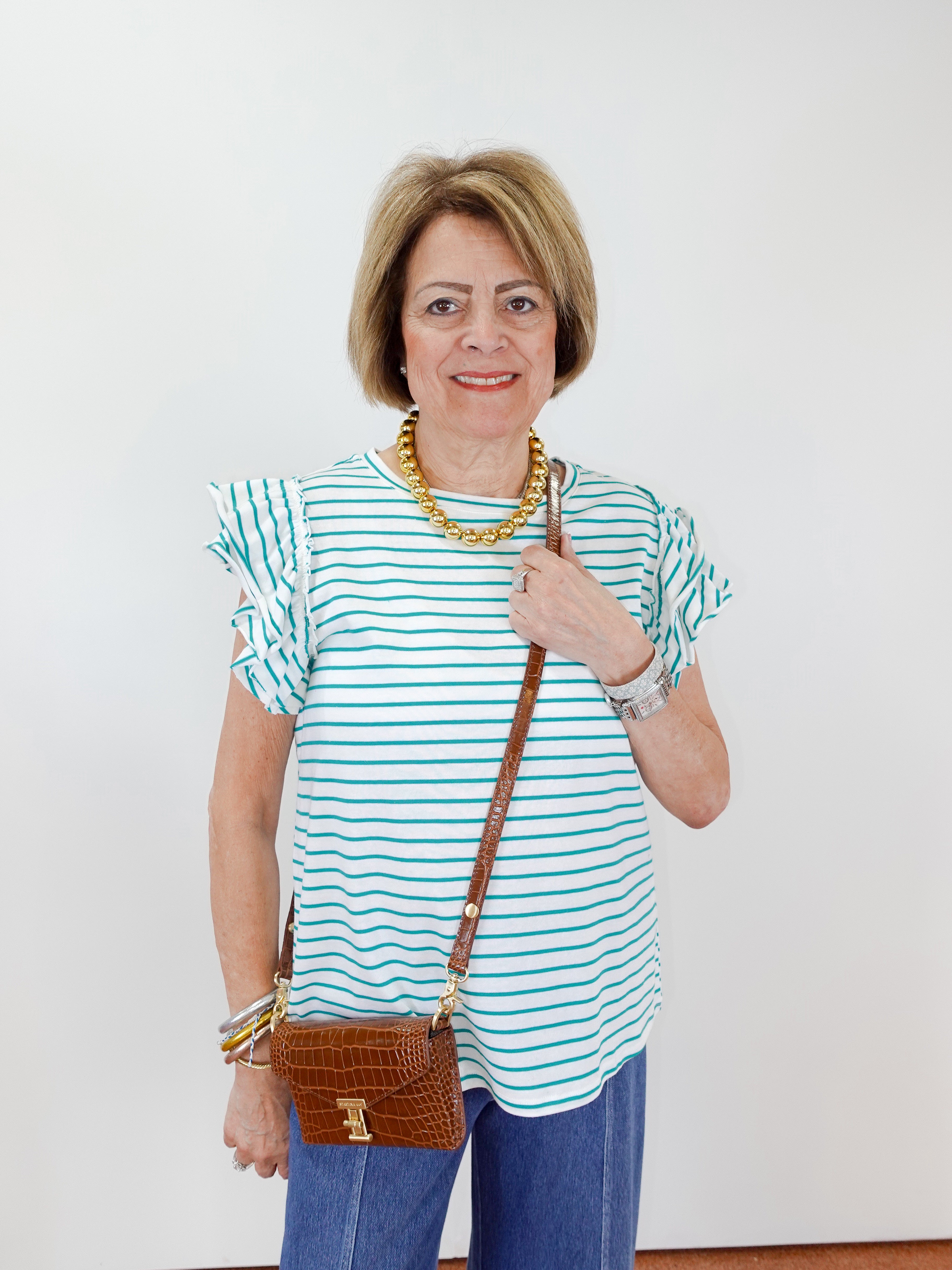 Woman wearing a striped shirt and holding a brown handbag against a white background
