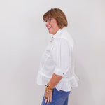 Person wearing a white blouse with ruffled sleeves and blue jeans against a plain background