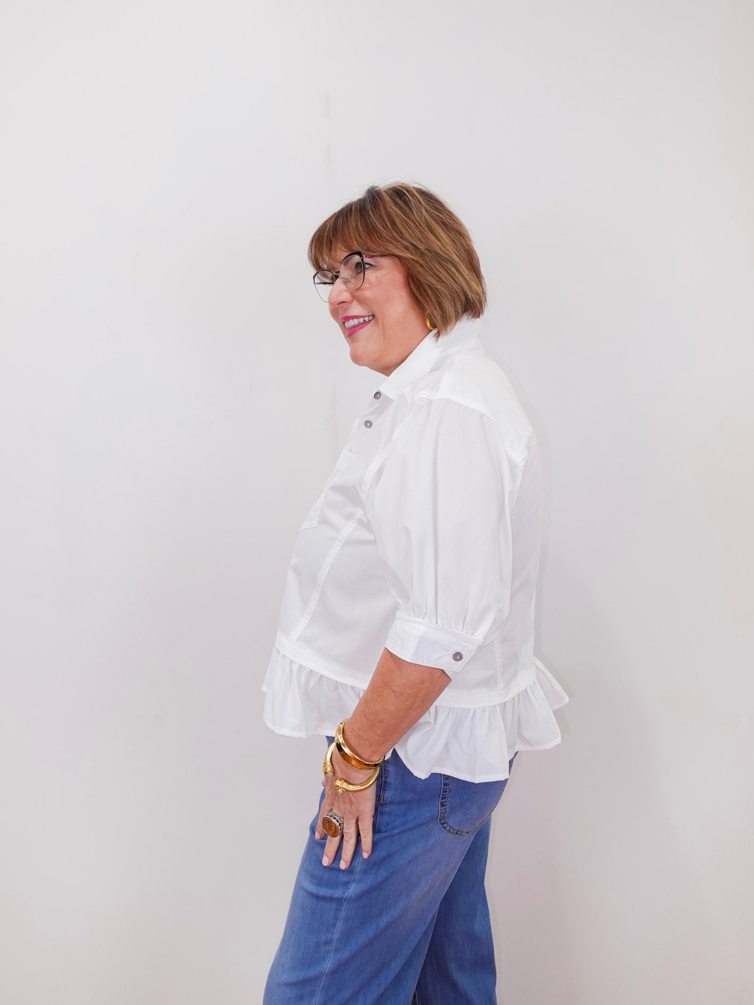 Person wearing a white blouse with ruffled sleeves and blue jeans against a plain background