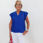 Woman wearing a blue blouse and white pants, holding a red bag against a white background