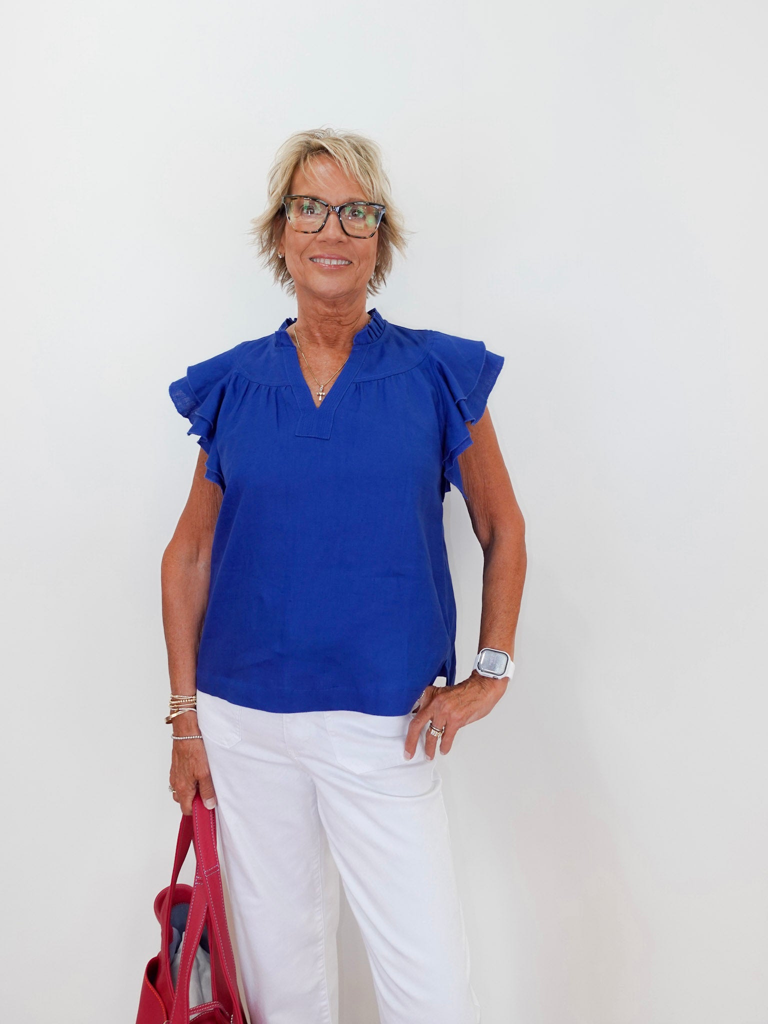 Woman wearing a blue blouse and white pants, holding a red bag against a white background