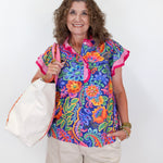 Woman wearing a colorful floral blouse and holding a white tote bag against a white background
