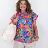Woman wearing a colorful floral blouse and holding a white tote bag against a white background