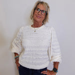 Woman wearing a textured white sweater and dark jeans against a plain background
