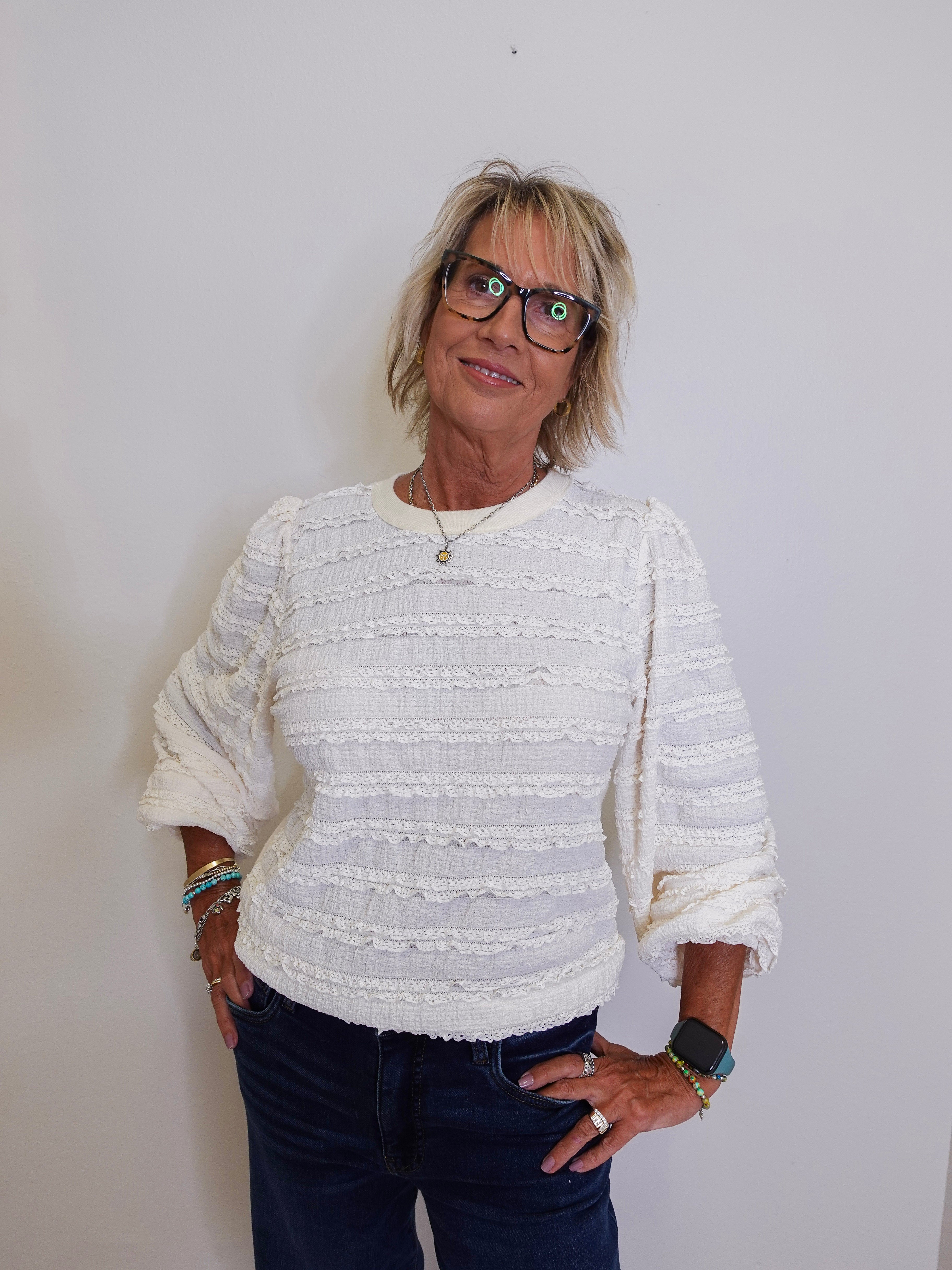 Woman wearing a textured white sweater and dark jeans against a plain background