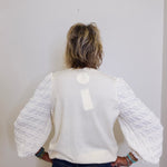 Person wearing a white textured sweater with long sleeves against a plain background