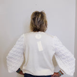 Person wearing a white textured sweater with long sleeves against a plain background