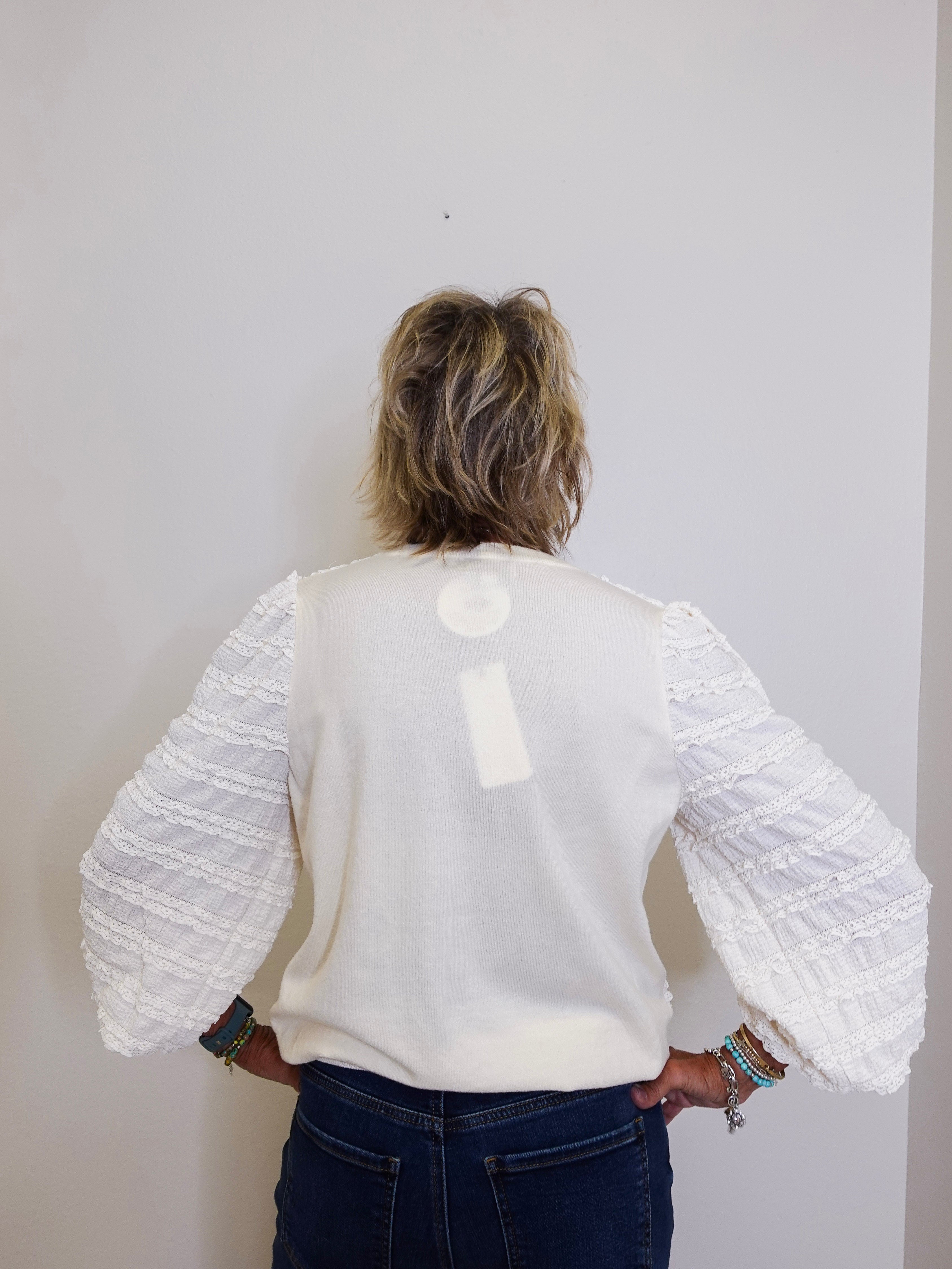 Person wearing a white textured sweater with long sleeves against a plain background