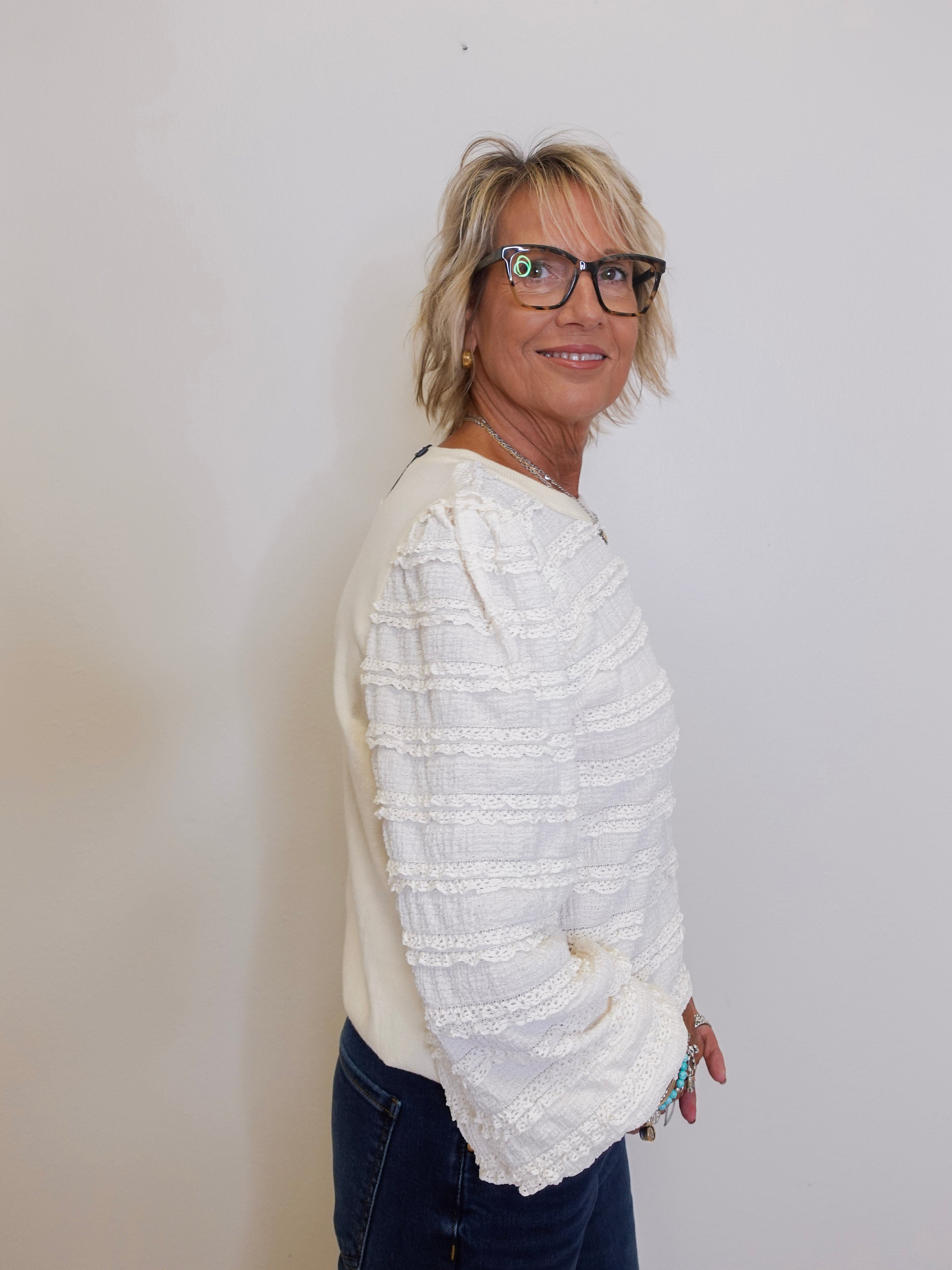 Woman wearing a white textured sweater and dark pants against a plain background
