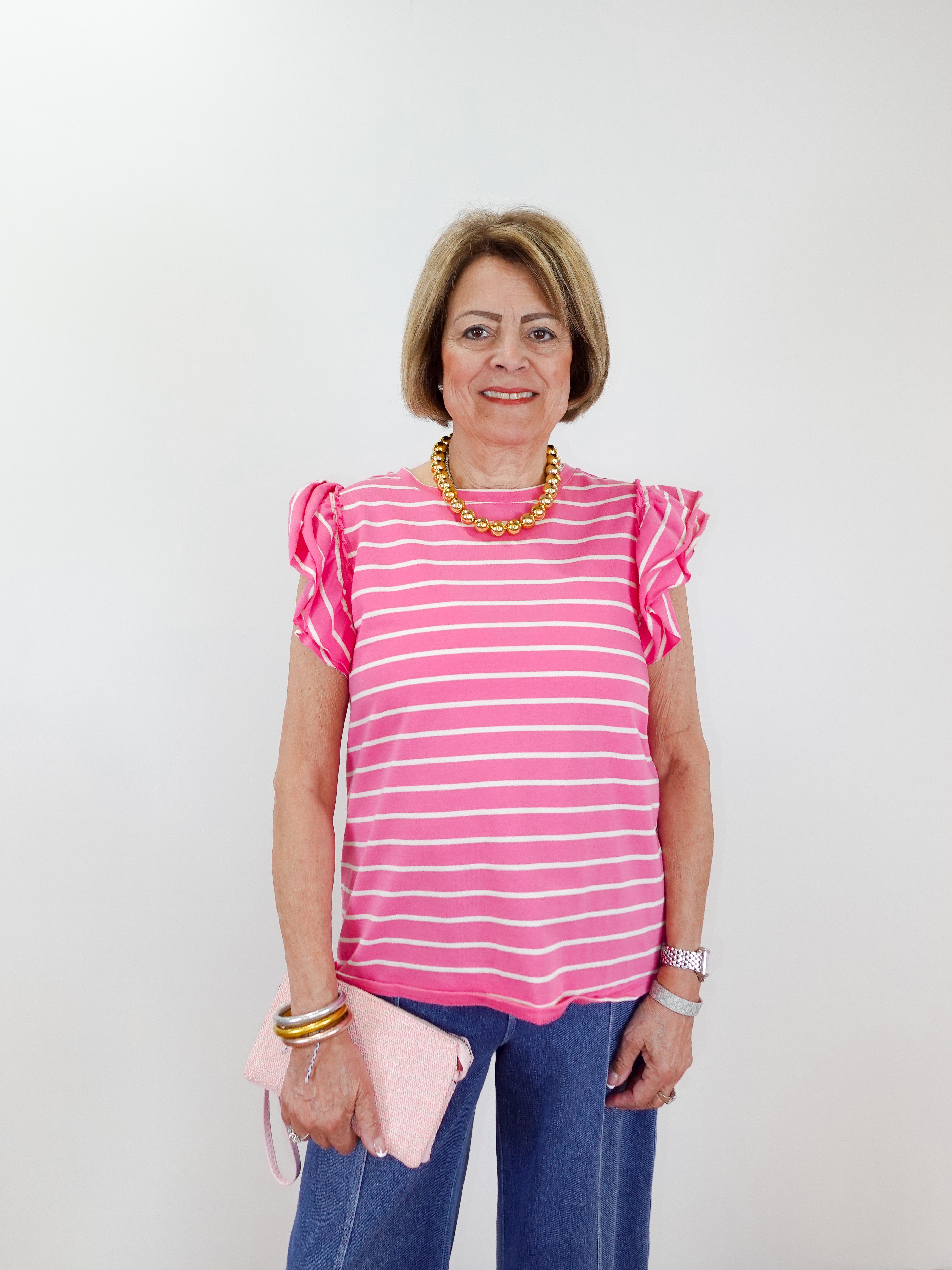 Woman wearing a pink and white striped shirt with ruffled sleeves against a plain background