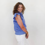 Woman wearing a blue shirt and white pants standing against a plain white background