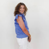 Woman wearing a blue shirt and white pants standing against a plain white background