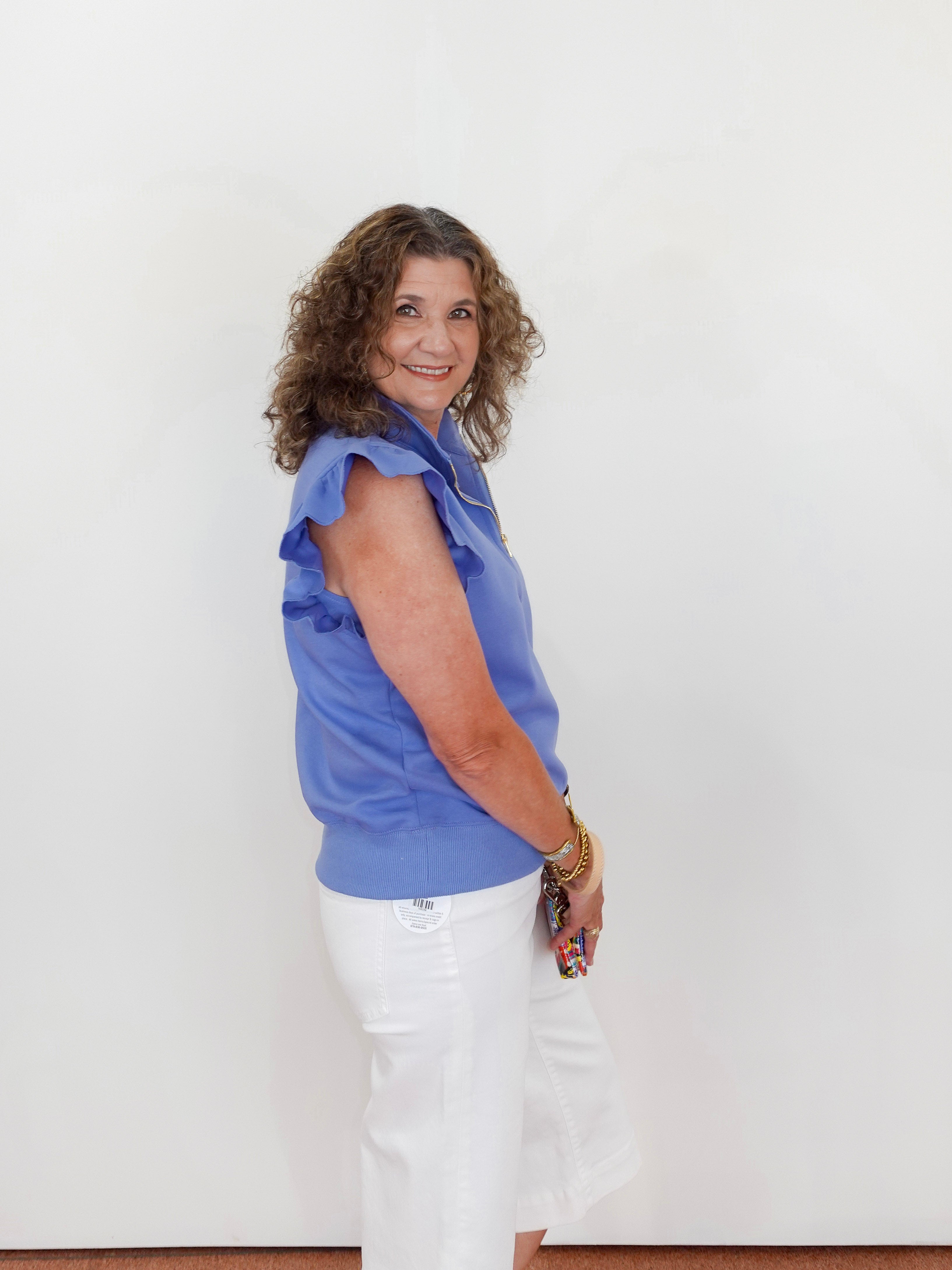 Woman wearing a blue shirt and white pants standing against a plain white background