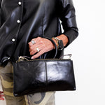 Person wearing a black leather jacket and holding a matching black leather clutch.