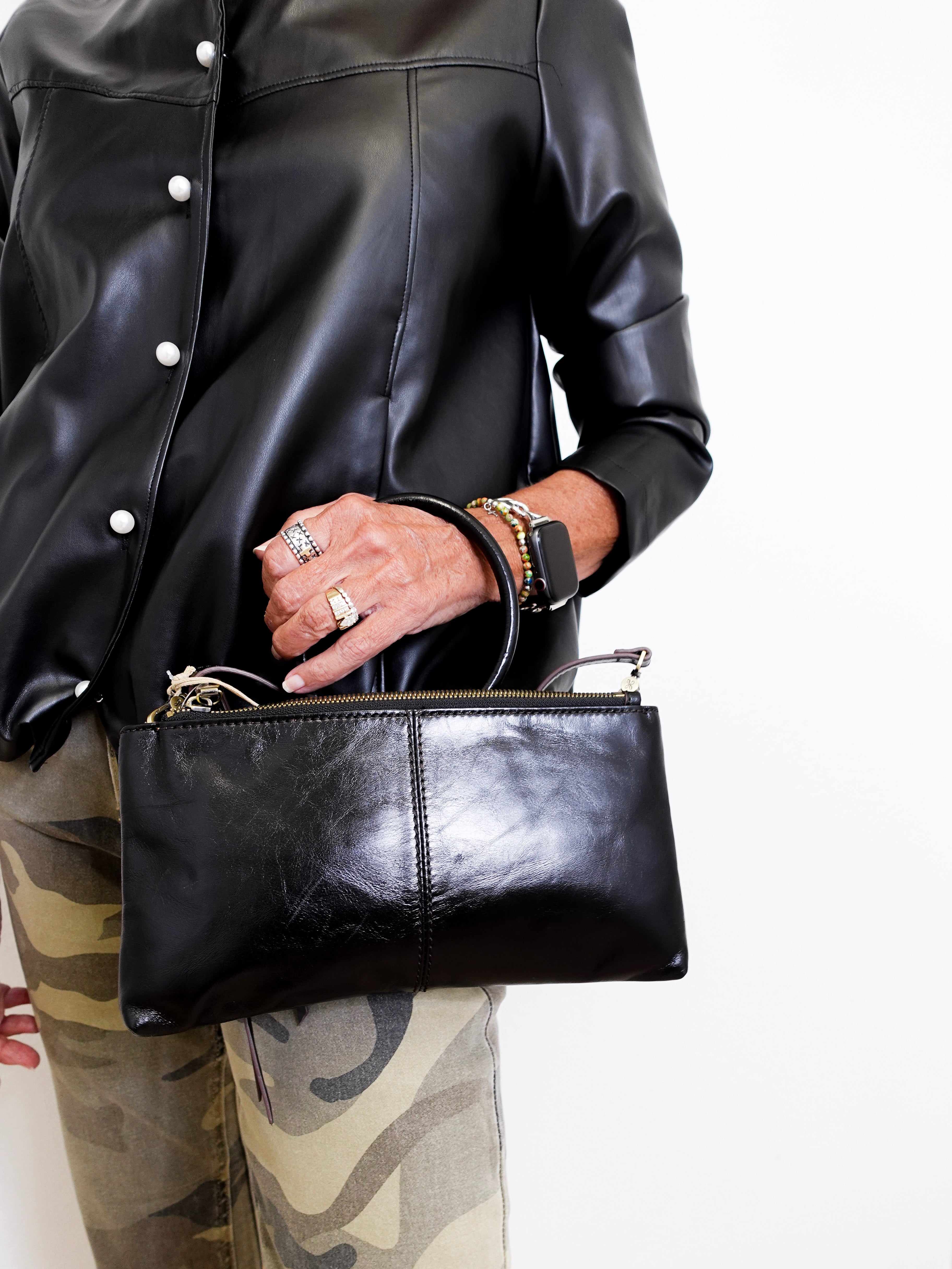 Person wearing a black leather jacket and holding a matching black leather clutch.