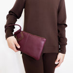 woman wearing the Maroon clutch bag with a ring handle on a light beige background