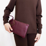 woman wearing the Maroon clutch bag with a ring handle on a light beige background