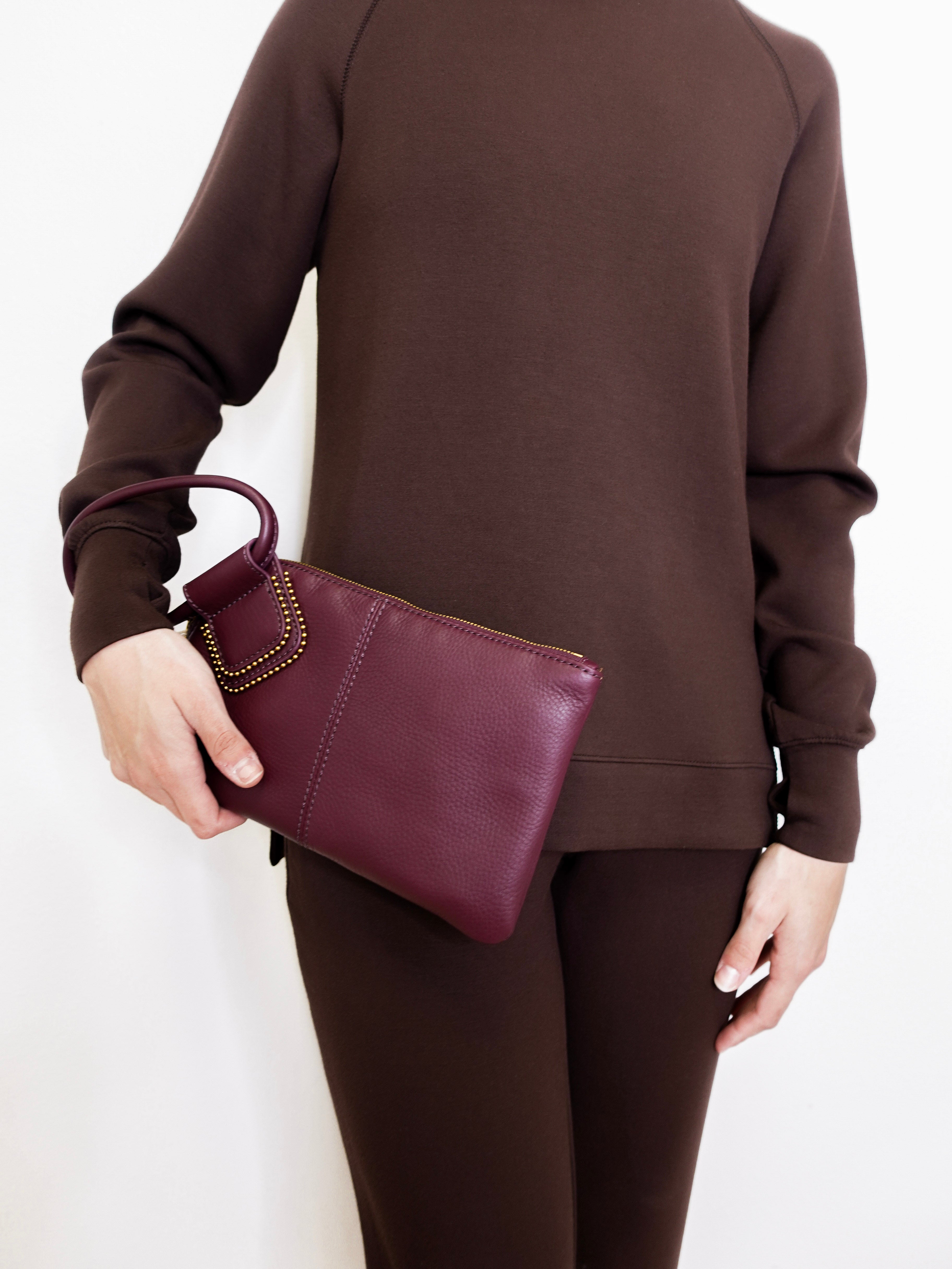 woman wearing the Maroon clutch bag with a ring handle on a light beige background