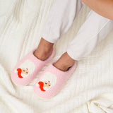 Pink slippers with cartoon face design worn by a person on a white textured surface