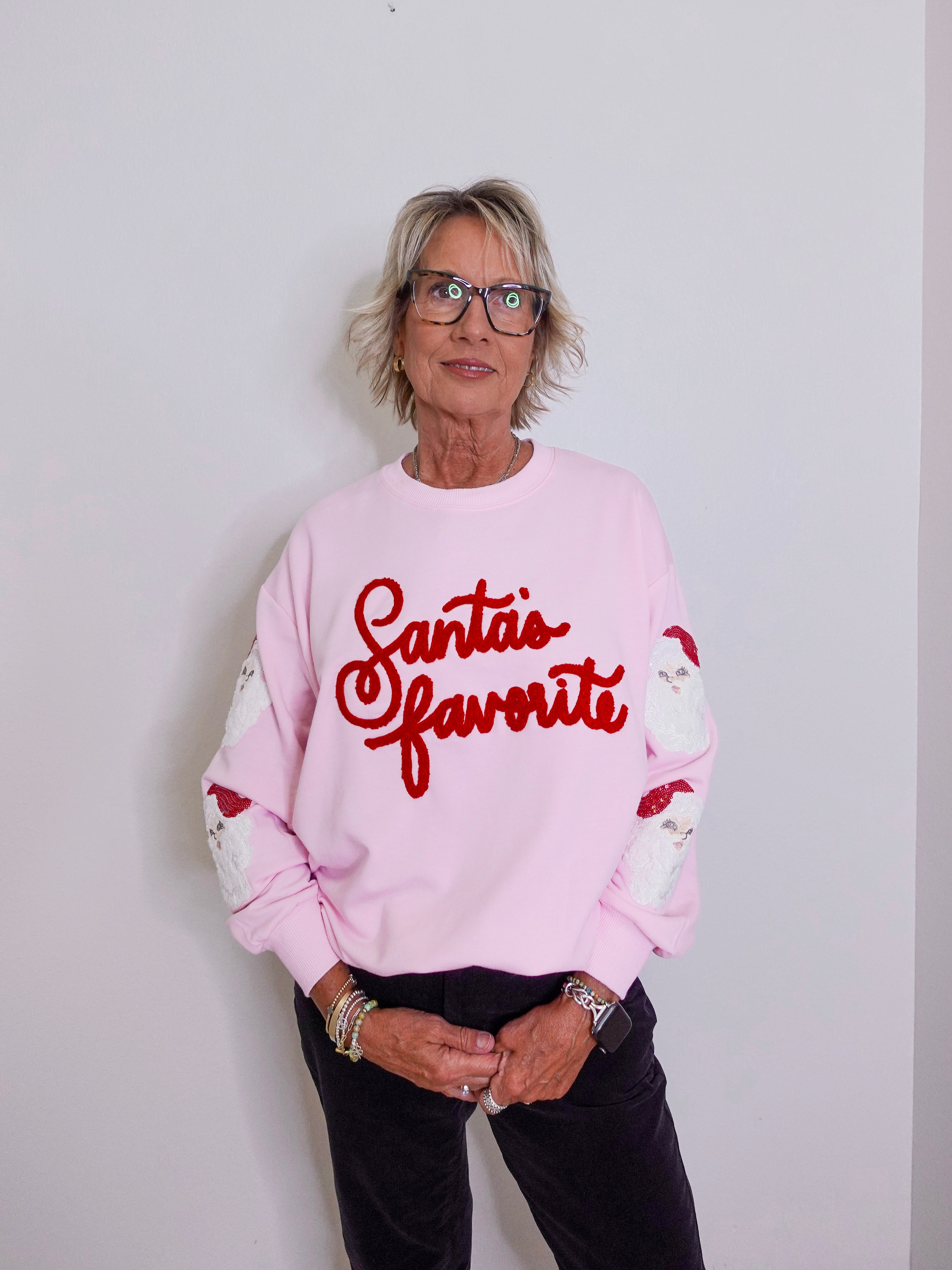 Person wearing a pink sweatshirt with 'Santa's favorite' text against a plain background