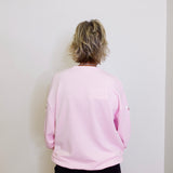 Person wearing a light pink sweatshirt against a white wall