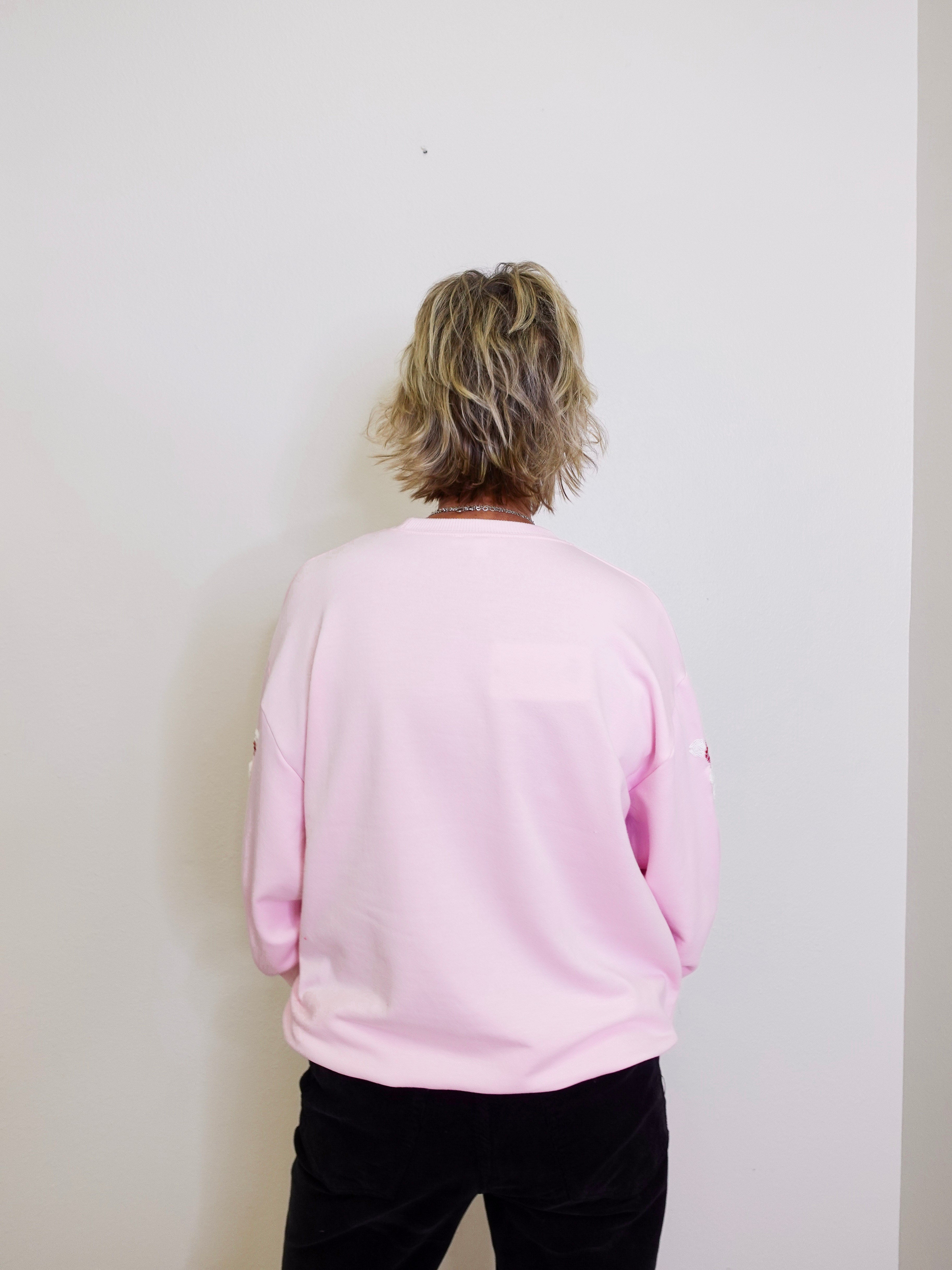 Person wearing a light pink sweatshirt against a white wall