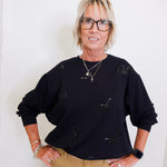 woman wearing a black sequin bat sweatshirt against a white wall. 