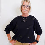 woman wearing a black sequin bat sweatshirt against a white wall. 
