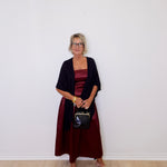 Woman wearing a dark red dress and black cardigan against a white wall.