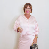 woman wearing a pink Karen Kane satin top against a white background. 