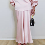 Woman modeling a pink satin mdi skirt against a white background. 