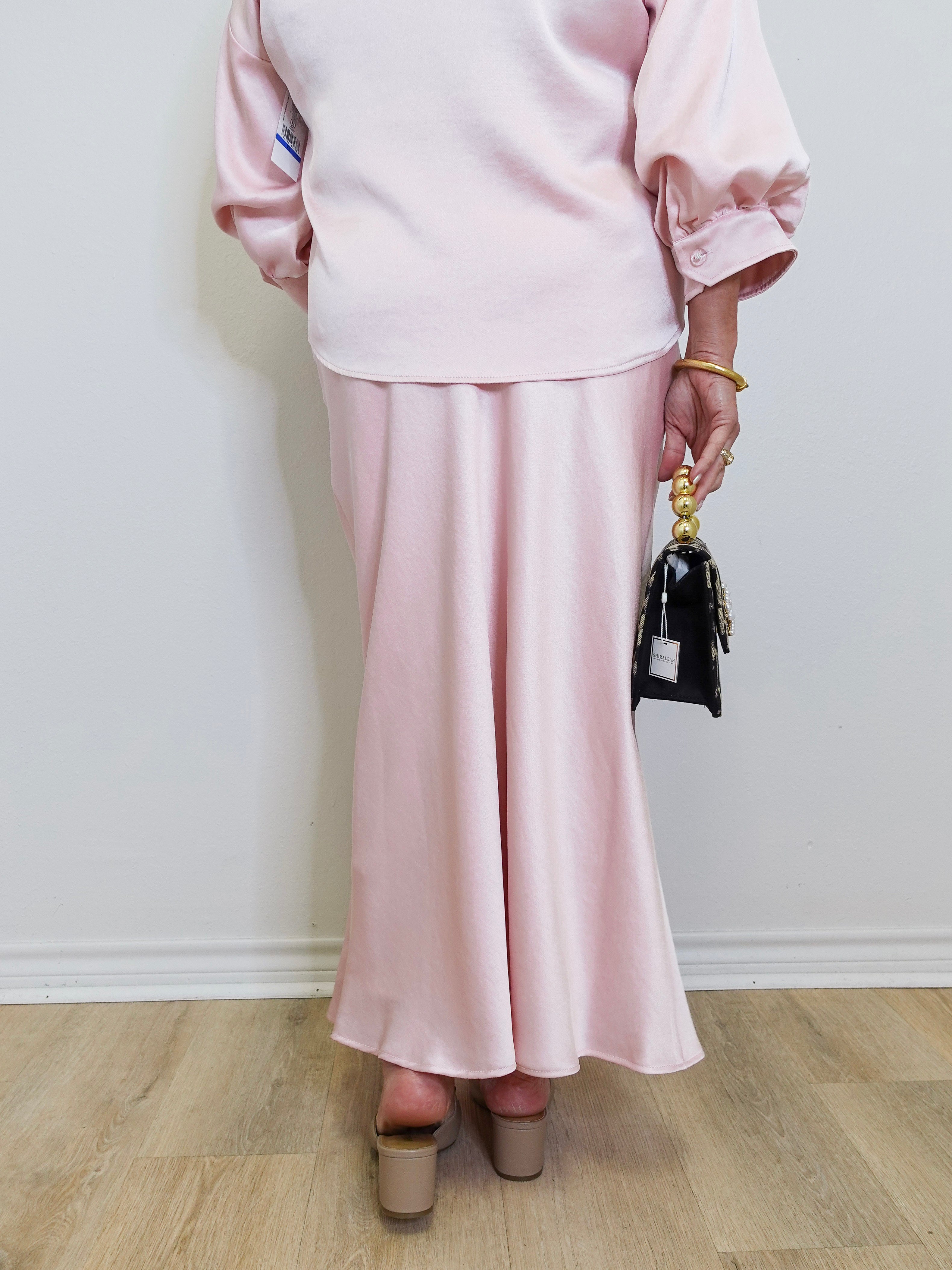 Woman modeling a pink satin mdi skirt against a white background. 