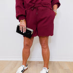 Person wearing a burgundy tracksuit with white sneakers on a light wooden floor.