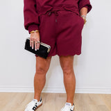 Person wearing a burgundy tracksuit with white sneakers on a light wooden floor.