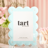 Light blue scalloped photo frame with 'tart by Taylor' branding on a blurred background.