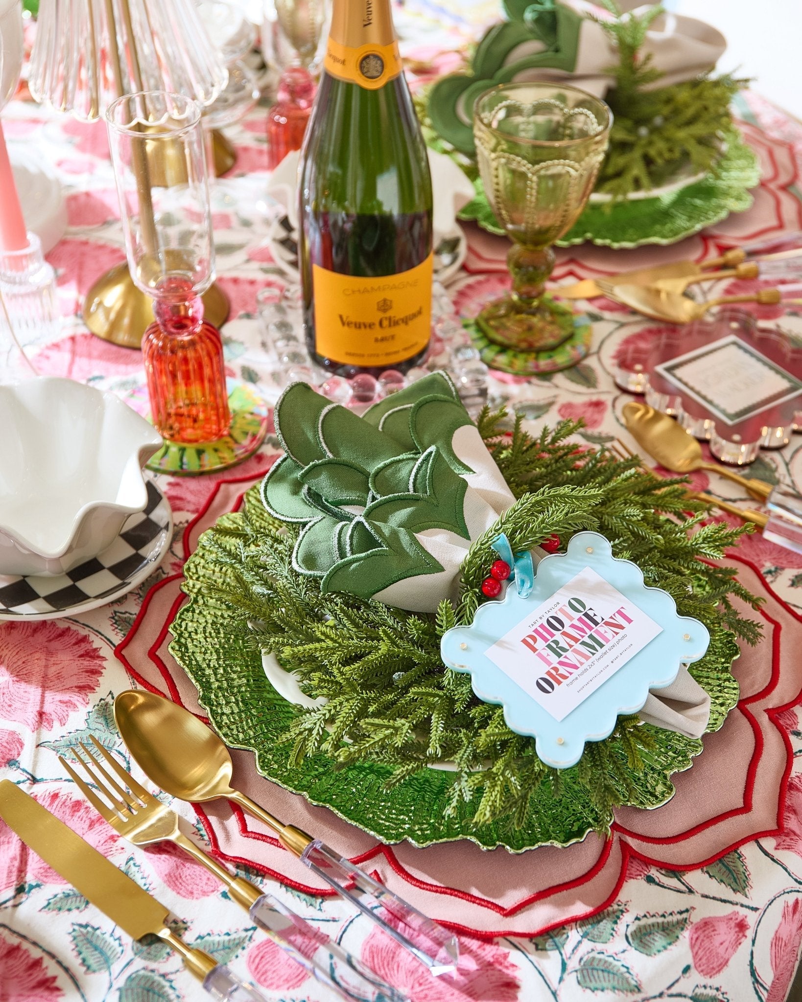 Decorative table setting with green wreath, wine bottle, and place card on a patterned tablecloth.