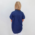 Person wearing a blue shirt standing against a white wall