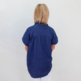 Person wearing a blue shirt standing against a white wall